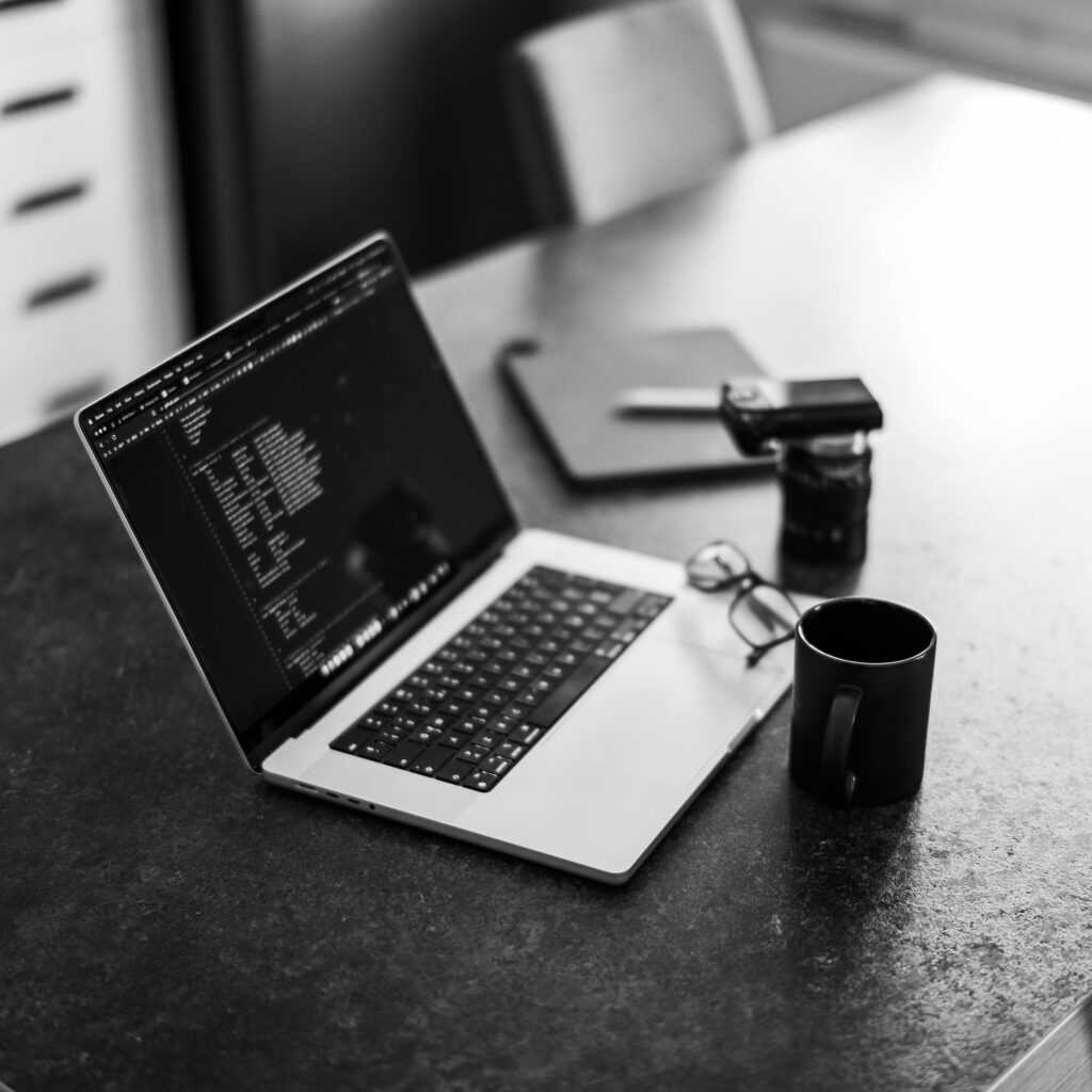 Black-and-white photo of a laptop on a table with coffee, perfect for remote work themes.