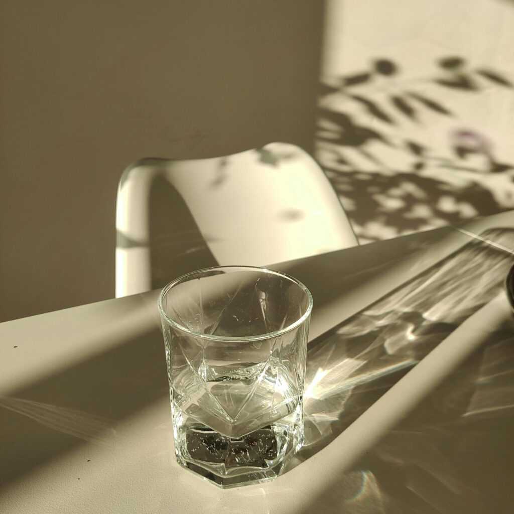 A minimalist scene of a glass of water casting shadows on a sunlit table.