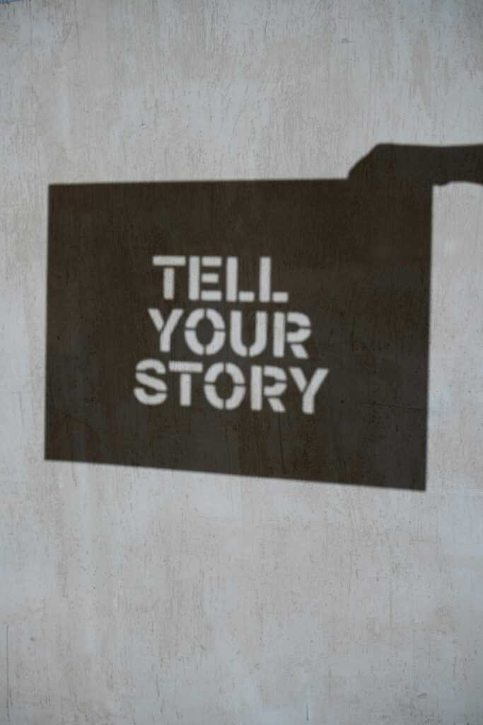 A shadow with the bold message 'Tell Your Story' cast on a concrete wall.