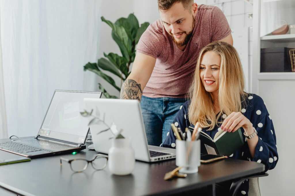 Two professionals collaborating at a desk with laptops in a bright, modern office.