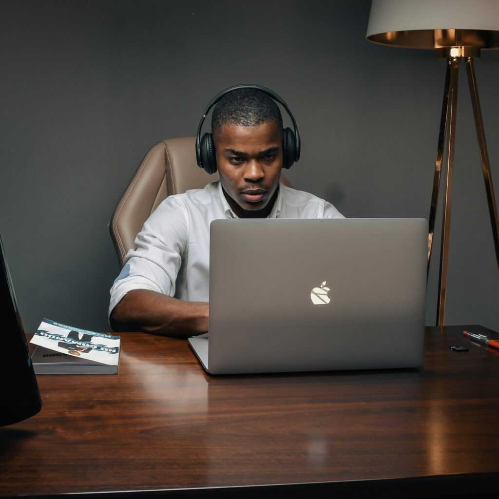 Professional man wearing headphones, working intently on a laptop in a modern office setting.